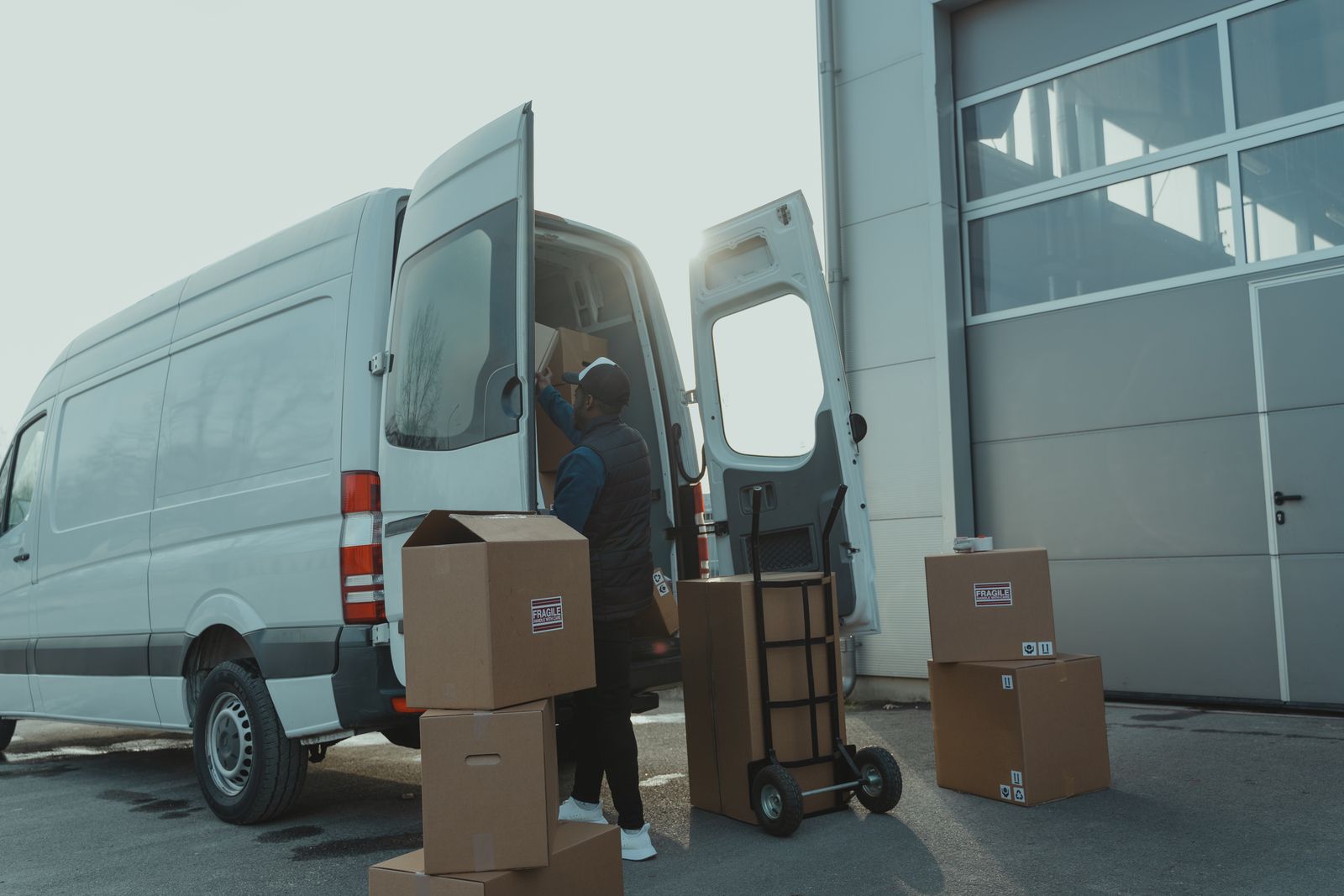 A courier loading parcels into a delivery van outside a warehouse